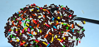 Colorful Chocolate Sprinkles With Spoon On White Surface