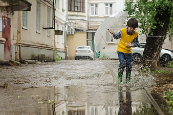Child jumping in puddle with umbrella on rainy street