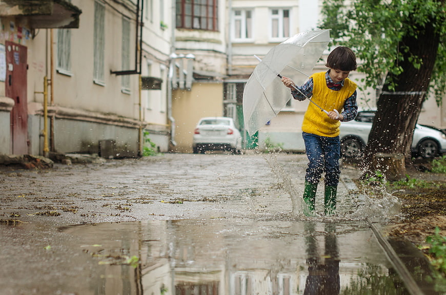 Child jumping in puddle with umbrella on rainy street