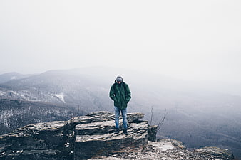 Hiker standing on rocky cliff edge overlooking snowy mountains