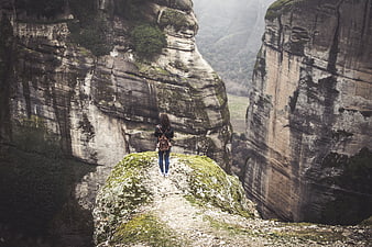 Woman hiking on rocky cliff edge in misty mountain landscape