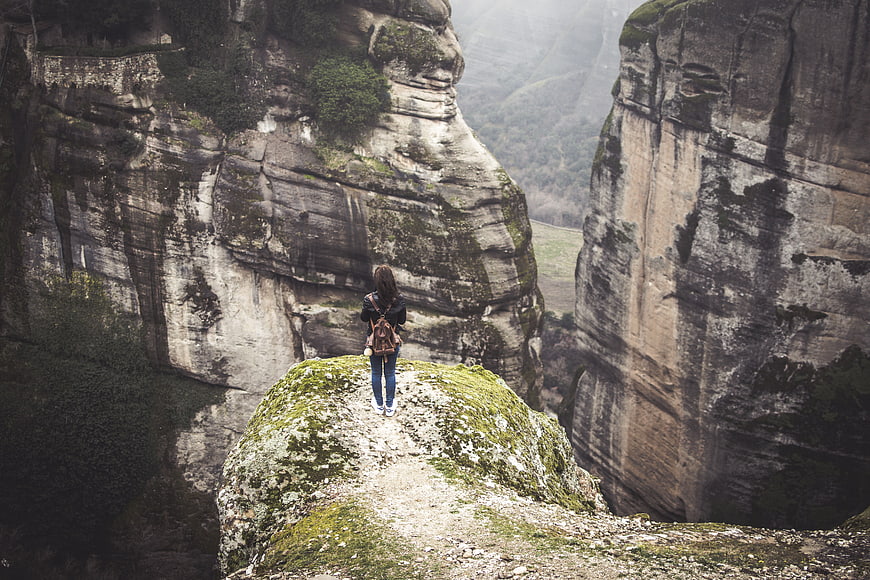 Woman hiking on rocky cliff edge in misty mountain landscape