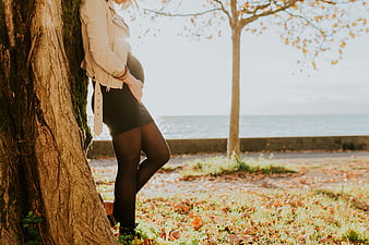 Pregnant woman leaning against tree in autumn park