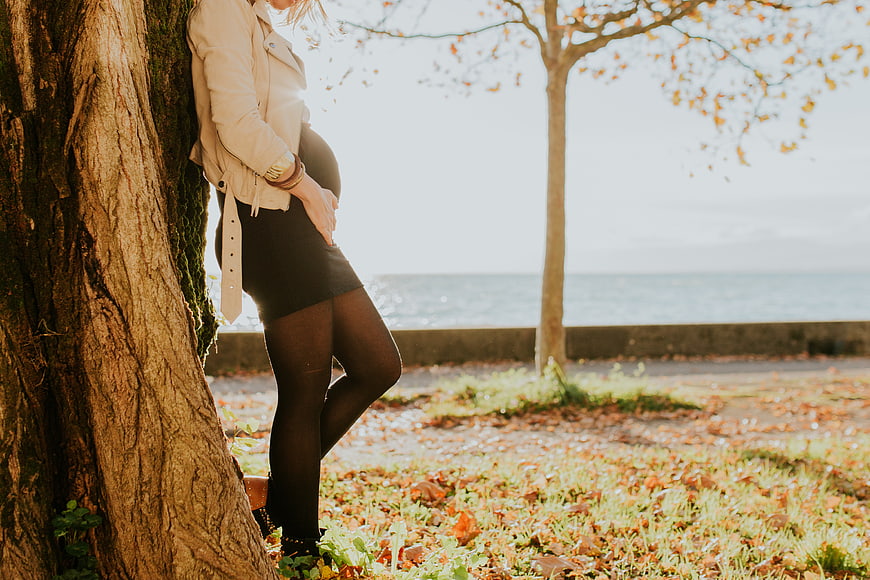 Pregnant woman leaning against tree in autumn park