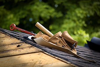 Leather tool belt with hammer on wooden roof shingles