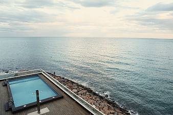 Modern infinity pool on wooden deck overlooking calm ocean