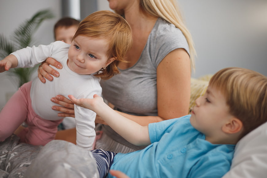 Mother playing with toddler and son on bed