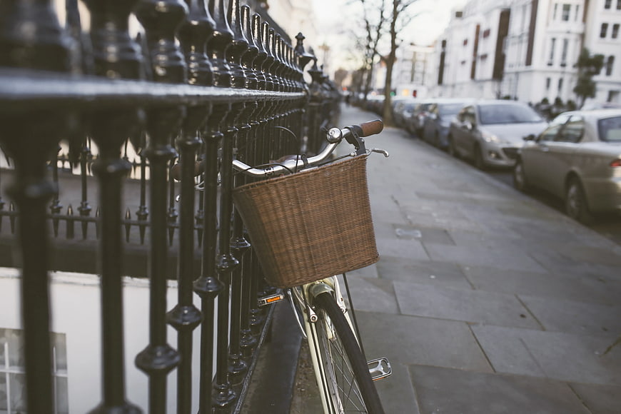 Silver Bicycle with Wicker Basket Leaning on Black Iron Fence