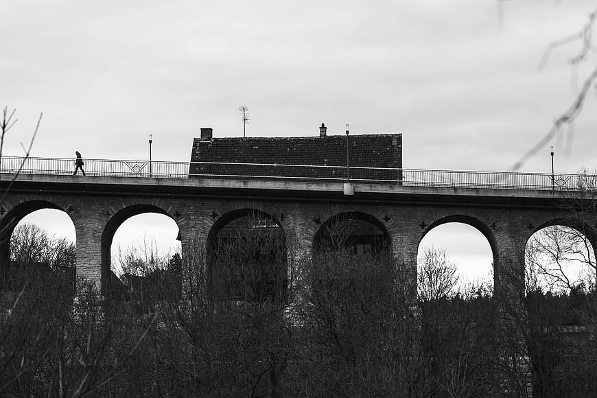 Black and white photo of stone viaduct with arches and pedestrian