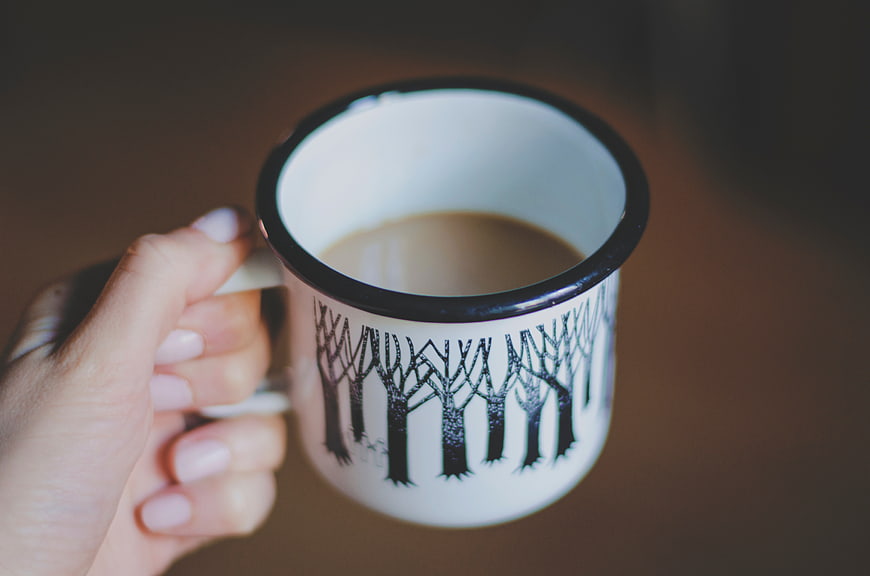 Hand holding white enamel mug with forest tree design
