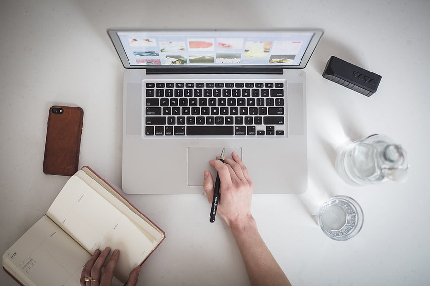 Top view of workspace with laptop, notebook, and water