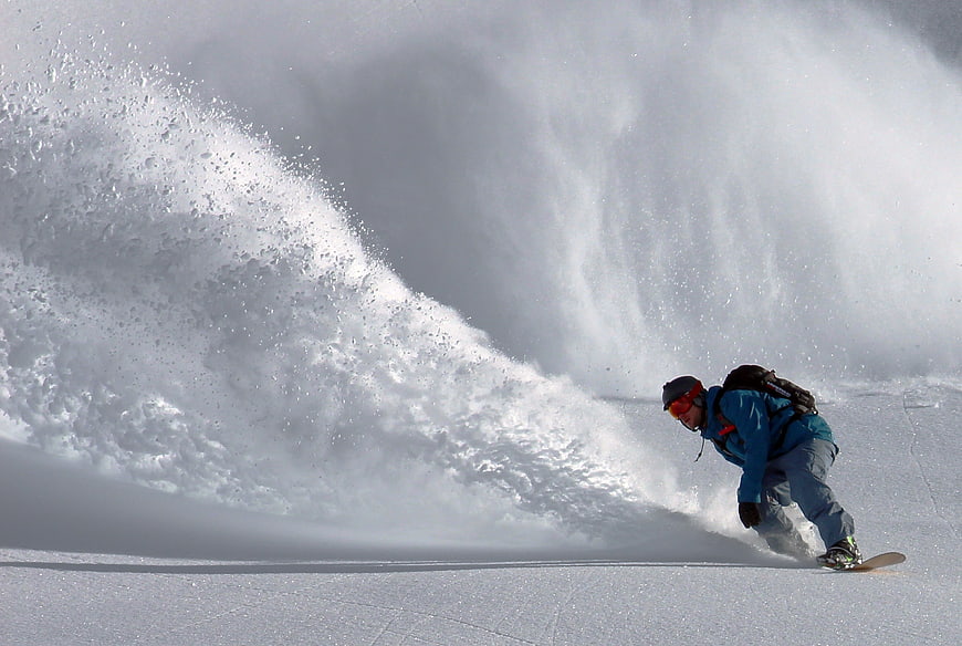 Snowboarder carving through deep powder snow on a mountain