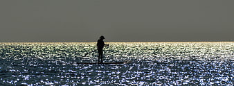 Silhouette of a woman paddle boarding on a sparkling ocean at sunrise