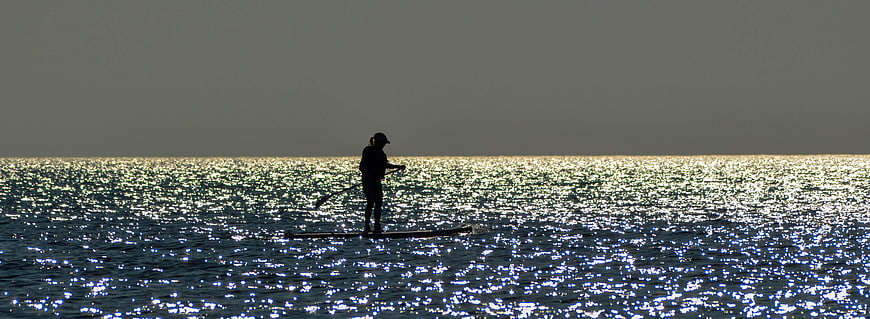 Silhouette of a woman paddle boarding on a sparkling ocean at sunrise