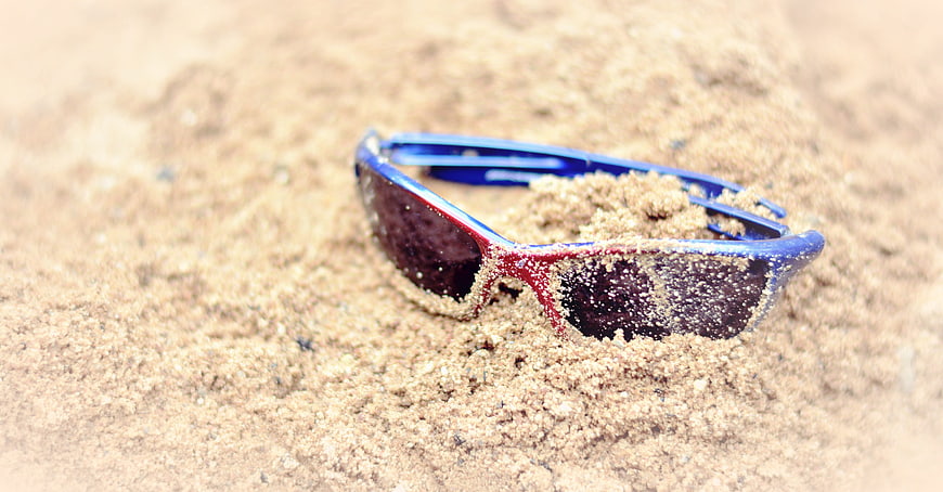 Blue and red sunglasses half buried in beach sand