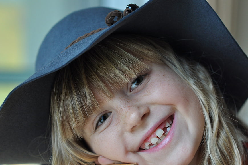 Close-up portrait of smiling girl with freckles and hat