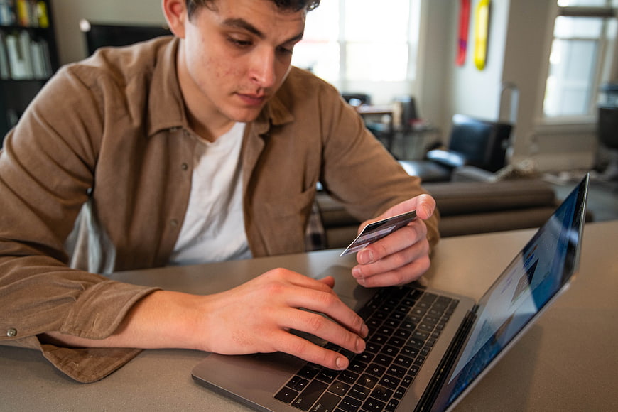 Young Man Online Shopping with Credit Card on Laptop