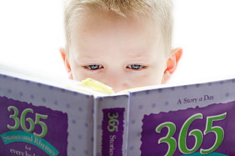 Cute young boy reading a 365 stories and rhymes book