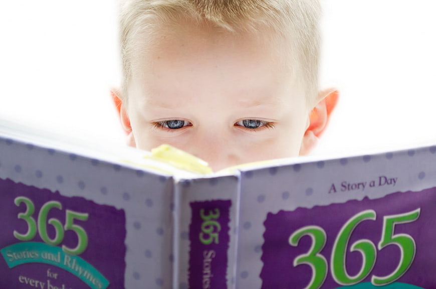 Cute young boy reading a 365 stories and rhymes book