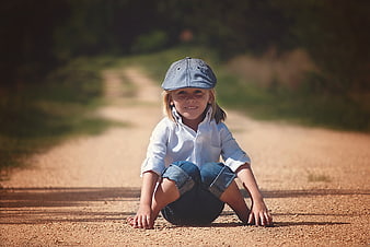 Smiling child sitting on a dirt road wearing a cap