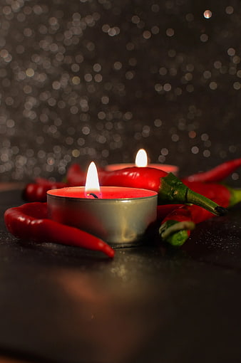 Red Chili Peppers with Lit Tealight Candle on Dark Background