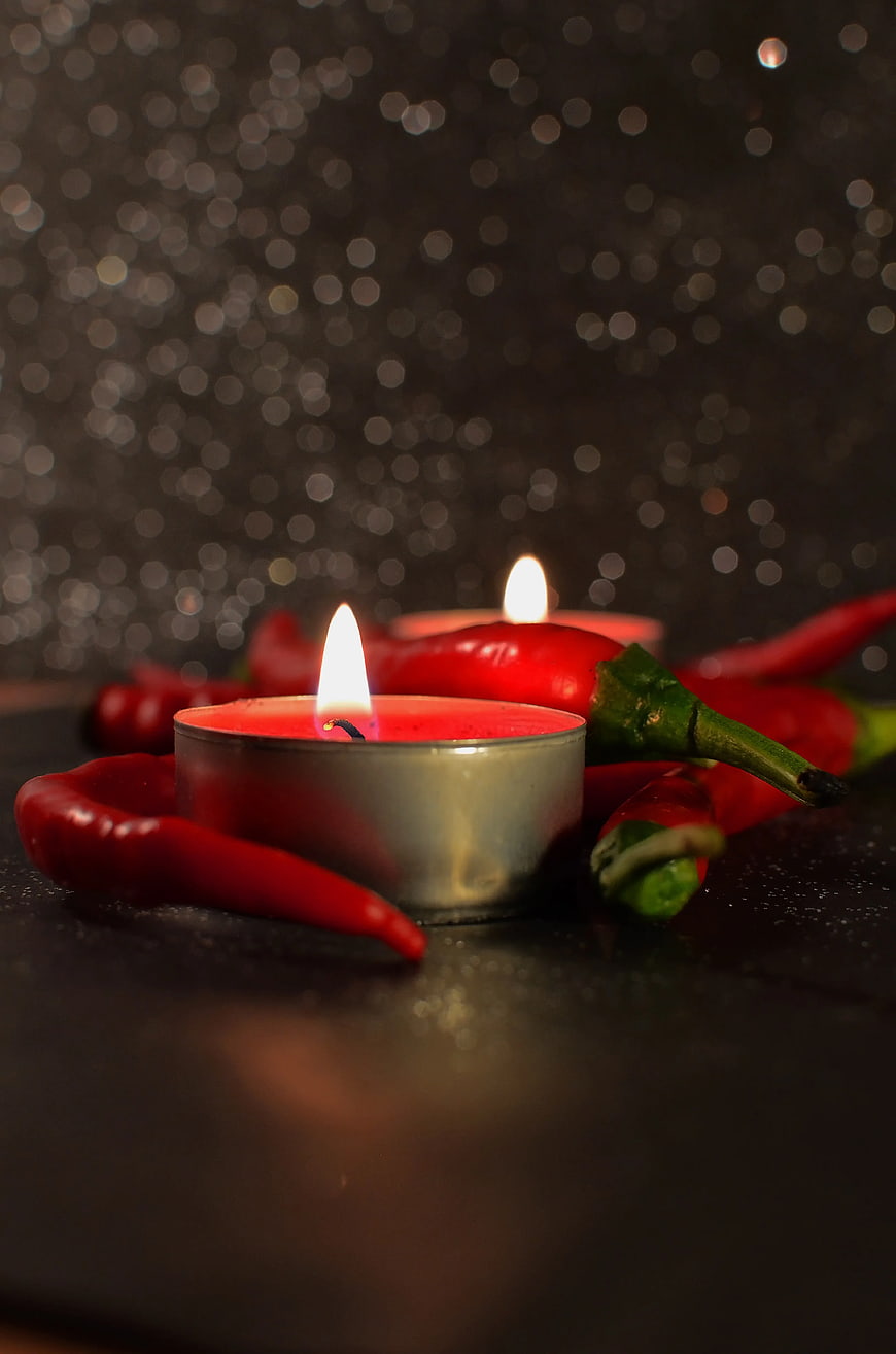 Red Chili Peppers with Lit Tealight Candle on Dark Background