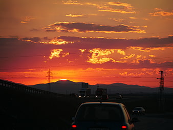 Vibrant orange sunset over highway with traffic and mountains