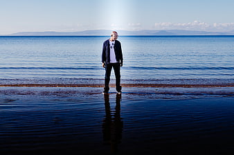 Man standing alone on wet beach with ocean reflection