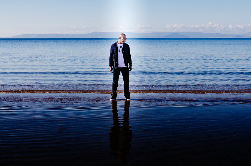 Man standing alone on wet beach with ocean reflection