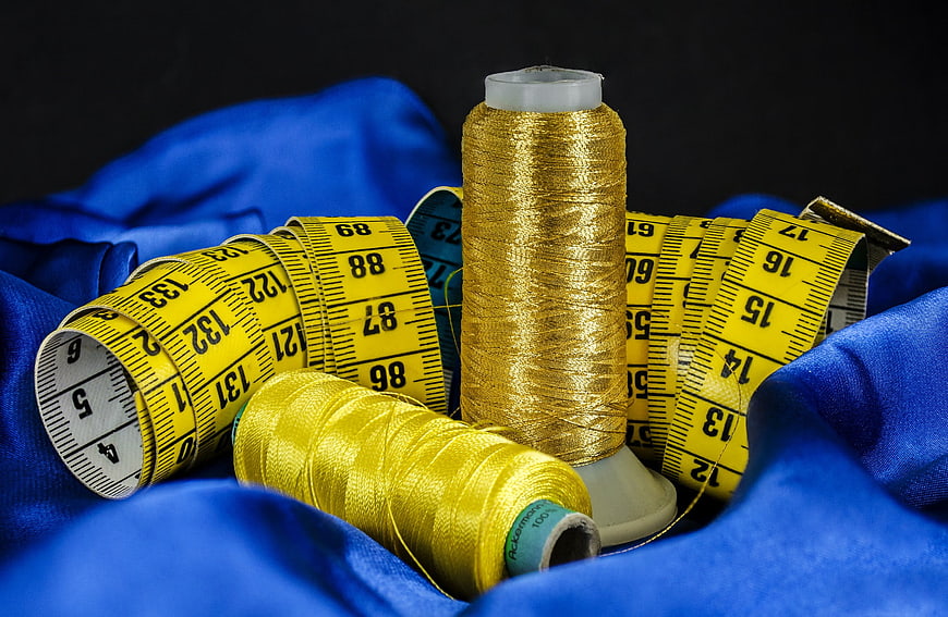 Gold thread spools and yellow measuring tape on blue fabric