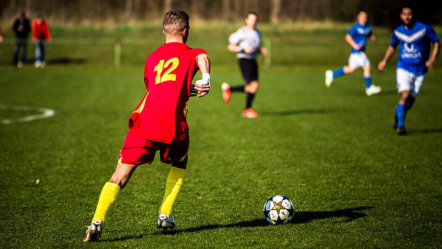 Soccer player in red jersey kicking ball on grass field
