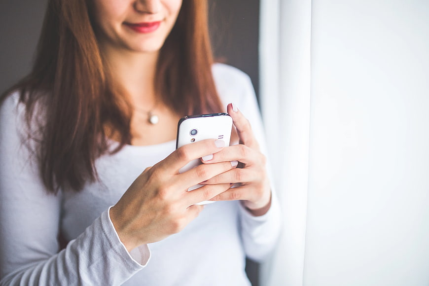 Young woman typing on smartphone by window