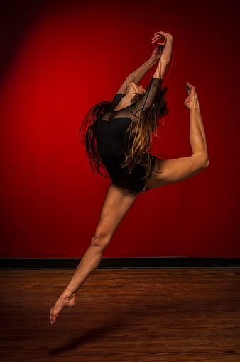 Female dancer leaping in black leotard against red background