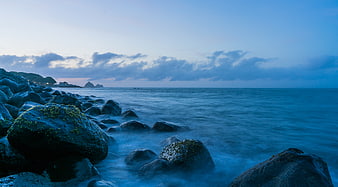 Serene Blue Ocean Coastline with Mossy Rocks at Dusk