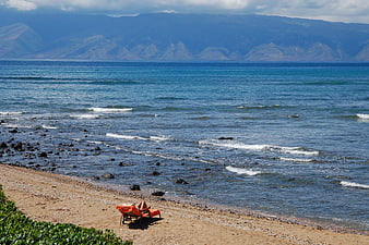 Solitary orange lounge chair on sandy beach with ocean and mountains