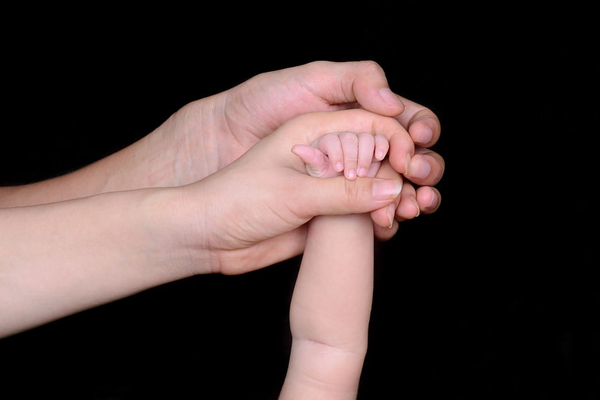 Adult Hands Holding Baby Hand on Black Background