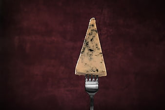 Wedge of blue cheese on a fork against dark red background