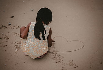 Little girl drawing heart in sand from behind