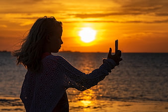 Silhouette of a girl taking a selfie at sunset by the ocean