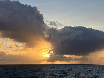 Dramatic sunset over ocean with golden sun rays breaking through dark clouds