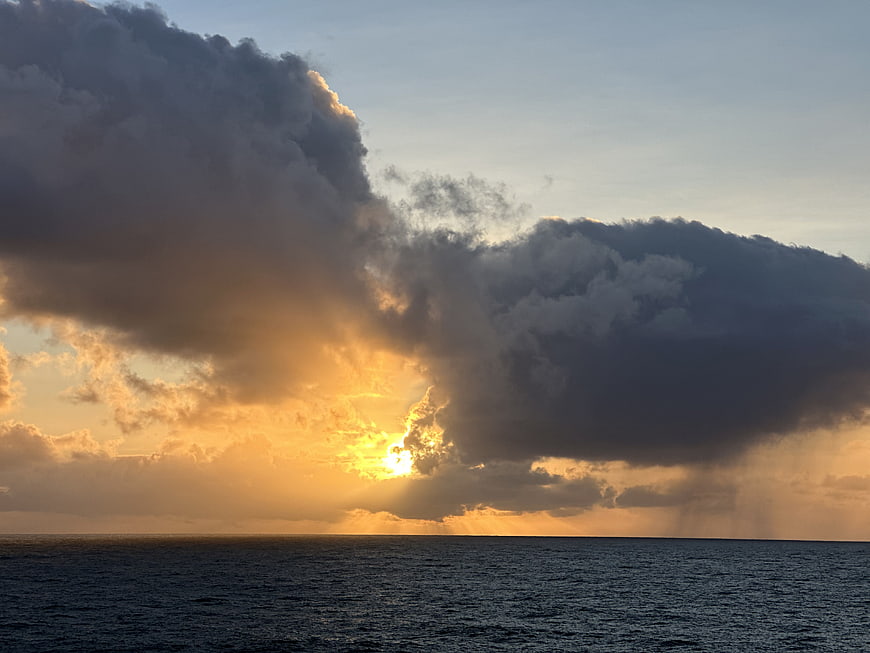 Dramatic sunset over ocean with golden sun rays breaking through dark clouds