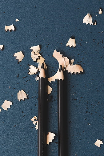 Two Black Pencils with Wood Shavings on Blue Background