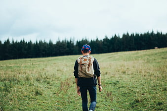 Man with Backpack Walking Through Green Meadow