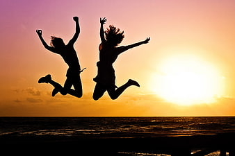 Silhouettes of two women jumping on beach at sunset