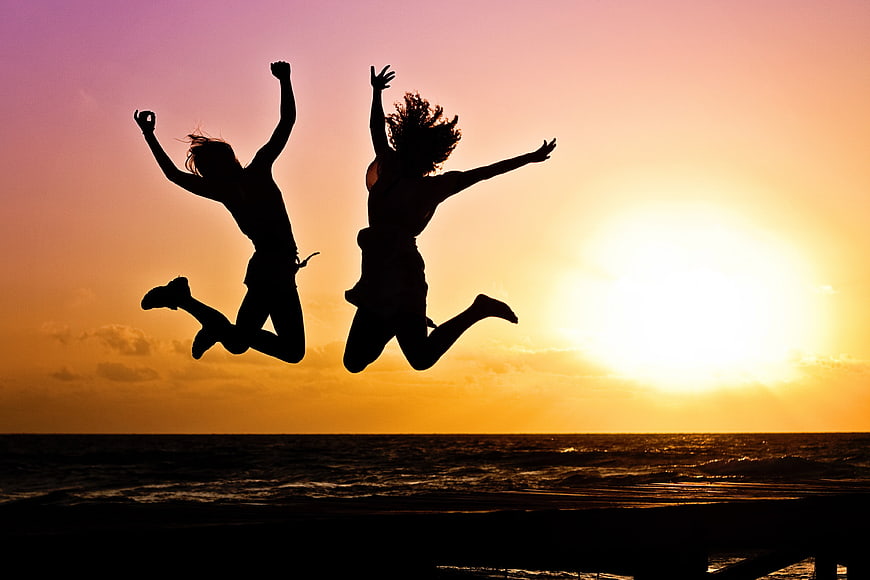 Silhouettes of two women jumping on beach at sunset