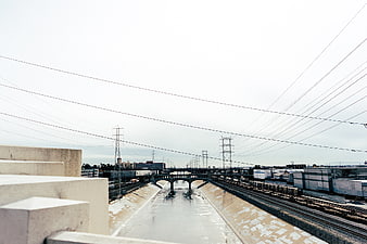 Urban concrete river channel with train tracks and power lines