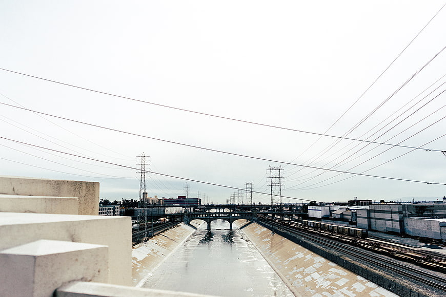 Urban concrete river channel with train tracks and power lines