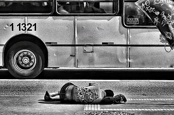 Black and white photo of homeless person sleeping on street near bus