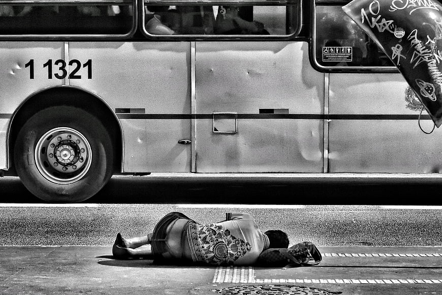 Black and white photo of homeless person sleeping on street near bus