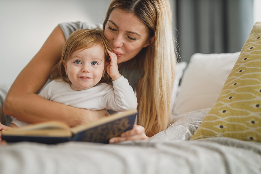 Mother reading book to toddler daughter in bed
